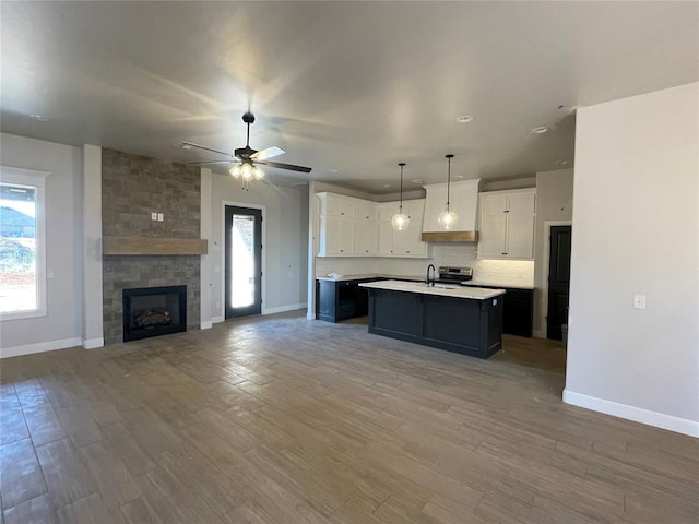 kitchen featuring hardwood / wood-style flooring, a large fireplace, an island with sink, white cabinets, and decorative light fixtures