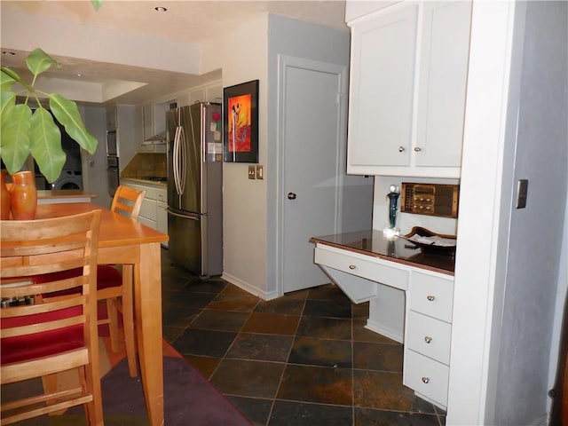 kitchen featuring stainless steel fridge, white cabinetry, washing machine and dryer, black cooktop, and wall chimney exhaust hood