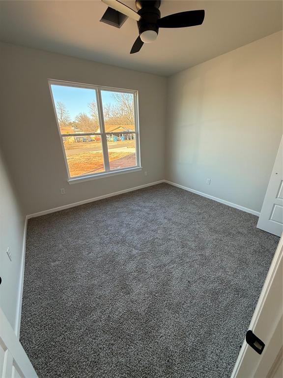 unfurnished room with ceiling fan and dark carpet