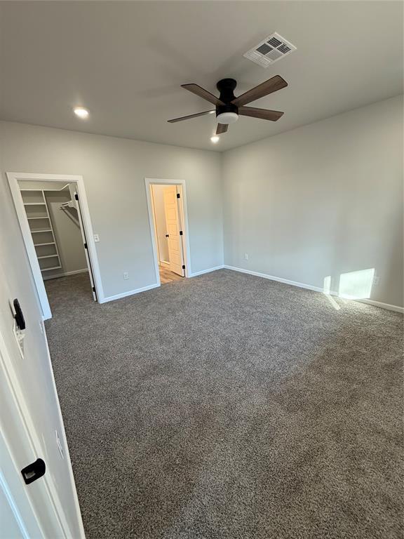 unfurnished bedroom with a walk in closet, dark carpet, ceiling fan, and a closet