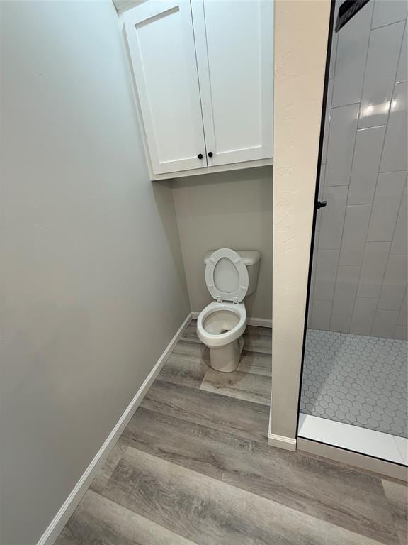 bathroom with hardwood / wood-style flooring, toilet, and tiled shower