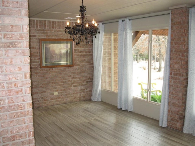 unfurnished dining area featuring a notable chandelier, wood-type flooring, and brick wall