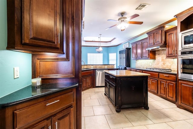 kitchen with a kitchen island, appliances with stainless steel finishes, backsplash, ceiling fan, and a tray ceiling