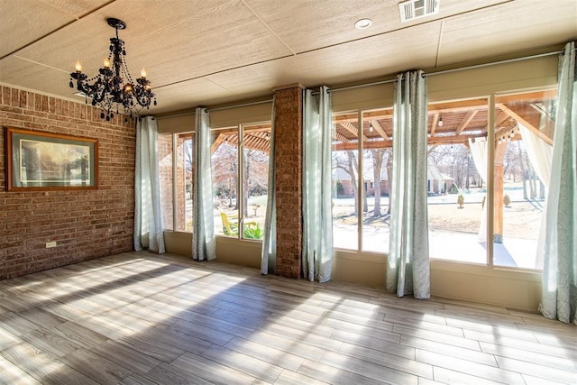 unfurnished room featuring brick wall, hardwood / wood-style floors, and a notable chandelier