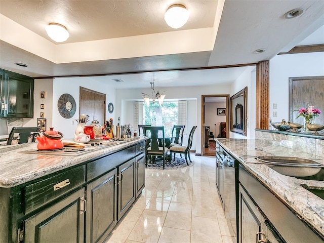 kitchen featuring stovetop, green cabinets, a center island, light stone counters, and a notable chandelier