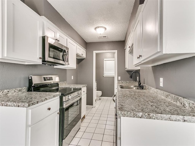 kitchen with sink, stainless steel appliances, a textured ceiling, white cabinets, and light tile patterned flooring