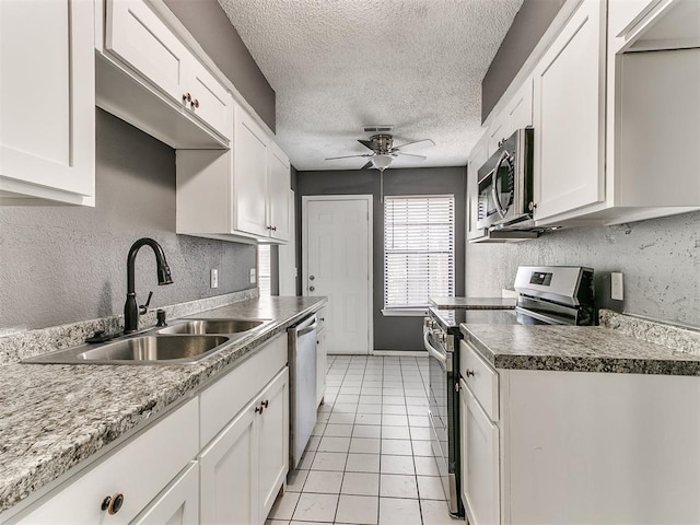 kitchen featuring sink, white cabinets, light tile patterned floors, stainless steel appliances, and a textured ceiling