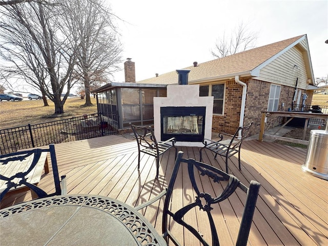 wooden deck with a sunroom and a multi sided fireplace