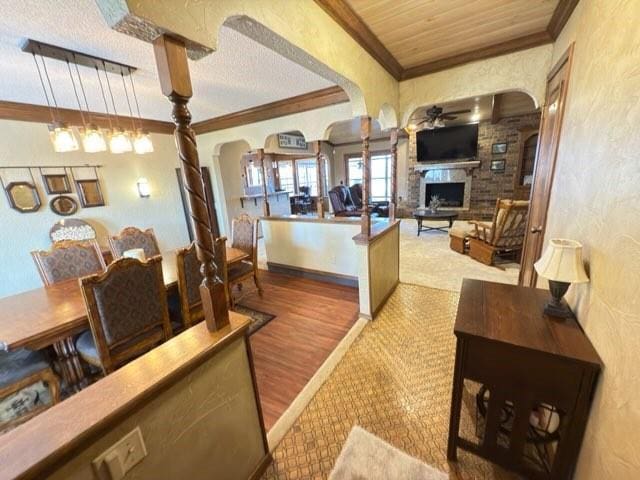 dining space featuring wood-type flooring, a stone fireplace, wood ceiling, and ceiling fan