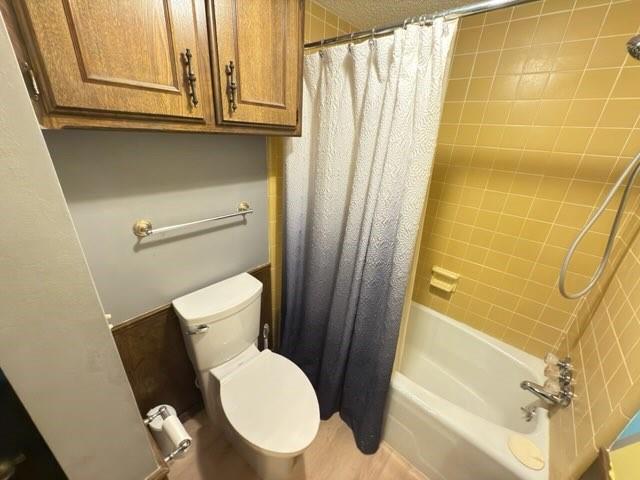 bathroom featuring shower / bathtub combination with curtain and toilet