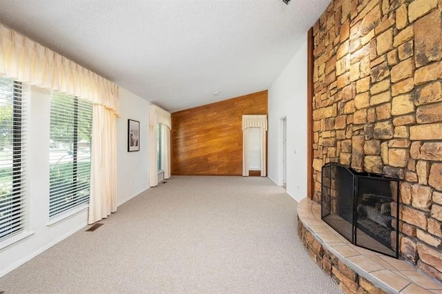 living room with a stone fireplace, wooden walls, lofted ceiling, light colored carpet, and a textured ceiling