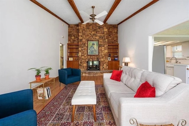 living room featuring built in shelves, a stone fireplace, a textured ceiling, dark hardwood / wood-style floors, and beam ceiling