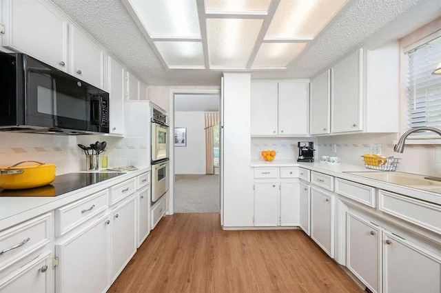 kitchen featuring white cabinetry, sink, backsplash, black appliances, and light hardwood / wood-style flooring