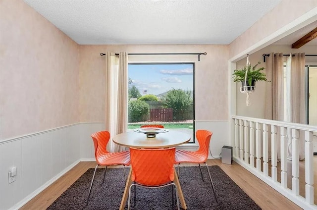 dining area featuring beamed ceiling, a textured ceiling, and light wood-type flooring