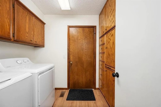 laundry room featuring separate washer and dryer, cabinets, a textured ceiling, and light wood-type flooring