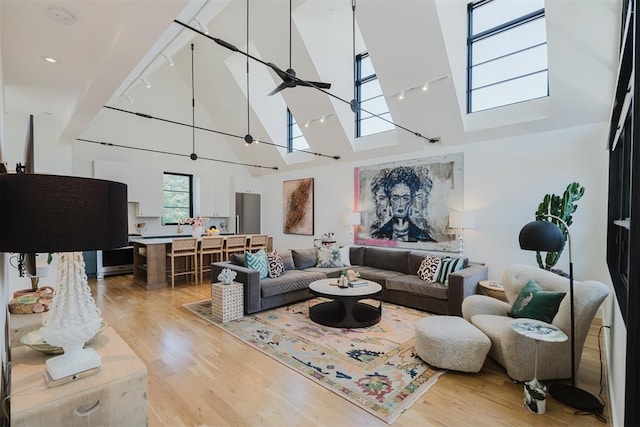 living room with high vaulted ceiling, a skylight, wood-type flooring, rail lighting, and ceiling fan