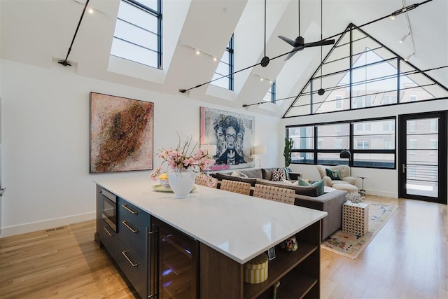 kitchen featuring high vaulted ceiling, built in microwave, beverage cooler, ceiling fan, and light wood-type flooring