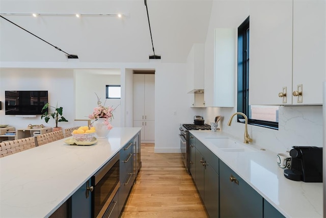 kitchen featuring sink, white cabinetry, light wood-type flooring, appliances with stainless steel finishes, and light stone countertops