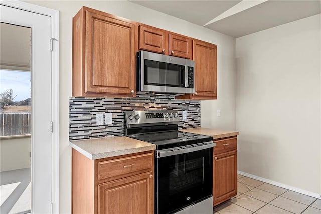 kitchen with brown cabinetry, light tile patterned flooring, light countertops, stainless steel appliances, and decorative backsplash
