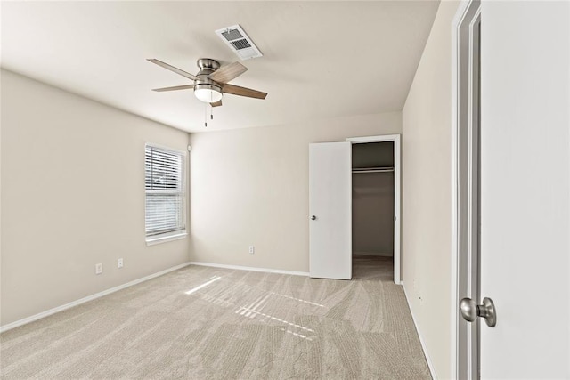 unfurnished bedroom with a ceiling fan, visible vents, light carpet, a walk in closet, and baseboards