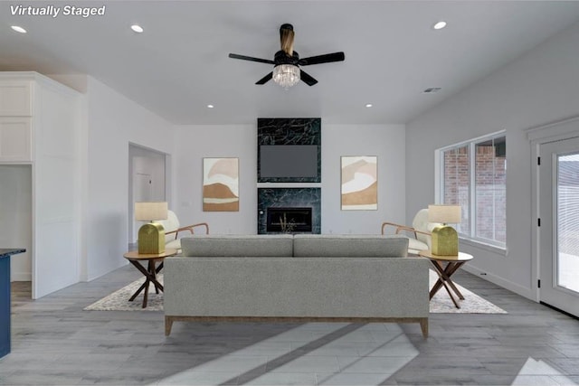 living room featuring a tile fireplace, ceiling fan, and light hardwood / wood-style flooring