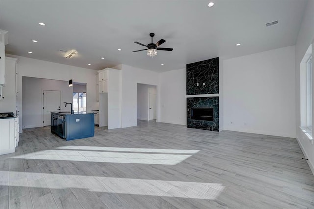 unfurnished living room with ceiling fan, sink, a high end fireplace, and light wood-type flooring