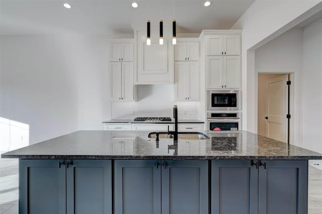 kitchen with dark stone countertops, a center island with sink, white cabinets, and appliances with stainless steel finishes