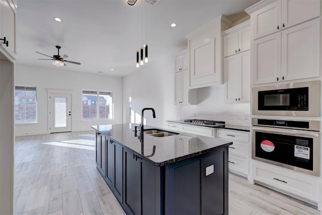 kitchen with appliances with stainless steel finishes, sink, white cabinets, dark stone counters, and a kitchen island with sink