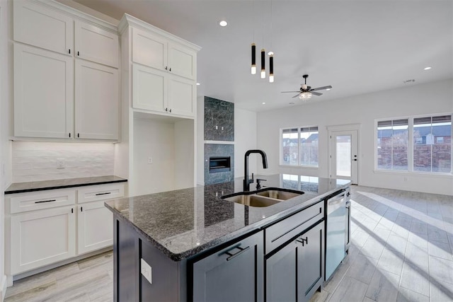 kitchen with sink, dark stone countertops, stainless steel dishwasher, an island with sink, and white cabinets