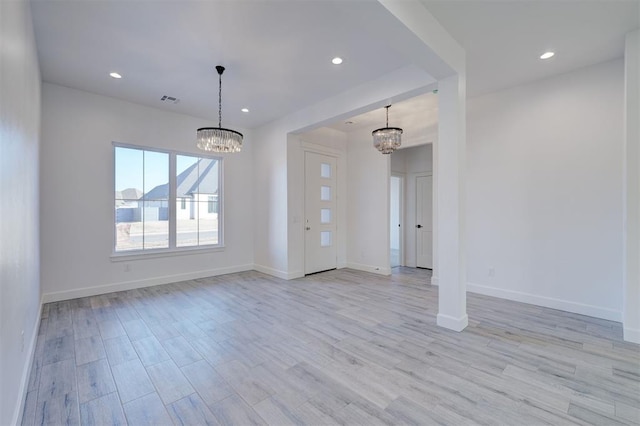 spare room featuring a notable chandelier and light wood-type flooring