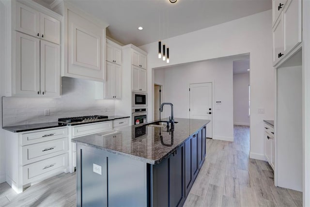 kitchen featuring sink, a center island with sink, dark stone counters, stainless steel appliances, and white cabinets