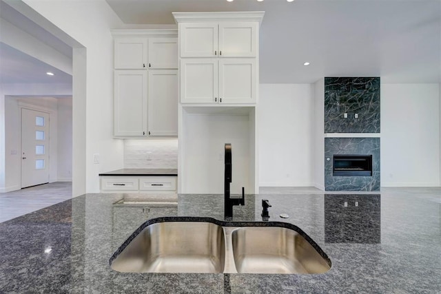 kitchen with sink, white cabinetry, dark stone countertops, a high end fireplace, and backsplash