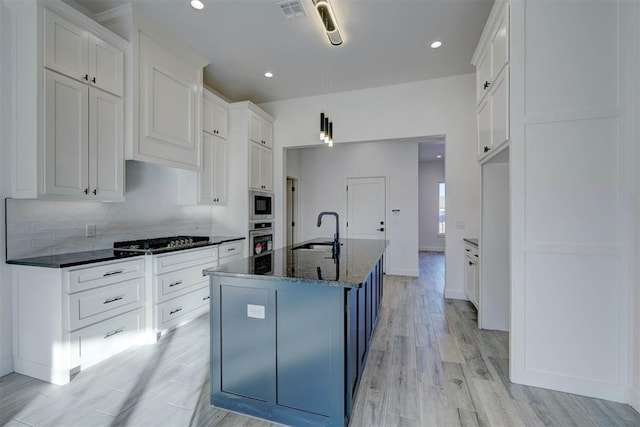 kitchen with sink, white cabinetry, a kitchen island with sink, dark stone countertops, and stainless steel appliances