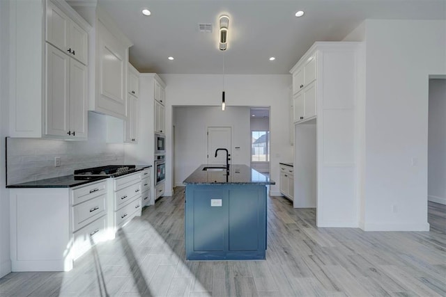 kitchen featuring sink, appliances with stainless steel finishes, white cabinets, a center island with sink, and dark stone counters