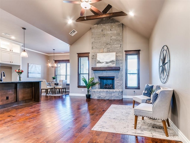 living room featuring a stone fireplace, high vaulted ceiling, beamed ceiling, ceiling fan, and dark wood-type flooring