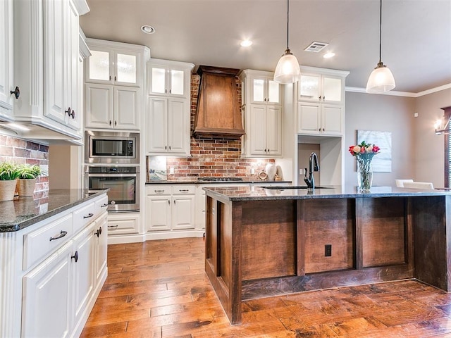 kitchen with decorative light fixtures, appliances with stainless steel finishes, custom range hood, dark stone counters, and white cabinets