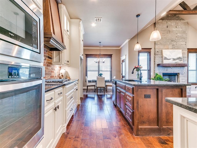 kitchen featuring decorative light fixtures, sink, a kitchen island with sink, stainless steel appliances, and custom range hood