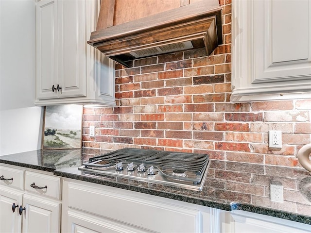 kitchen with premium range hood, stainless steel gas cooktop, dark stone countertops, and white cabinets