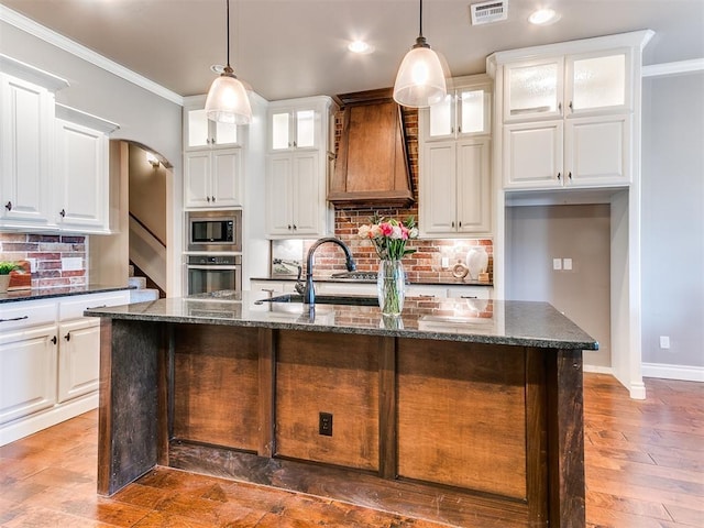 kitchen with stainless steel appliances, a kitchen island with sink, white cabinets, and custom range hood