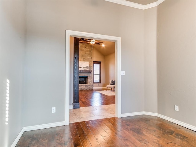 unfurnished room featuring hardwood / wood-style flooring, crown molding, a stone fireplace, and ceiling fan