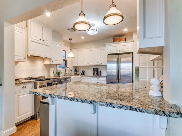 kitchen with pendant lighting, a breakfast bar area, white cabinets, light stone counters, and stainless steel appliances