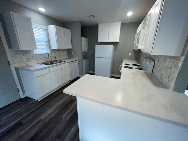 kitchen with sink, white appliances, white cabinetry, stacked washer / dryer, and kitchen peninsula