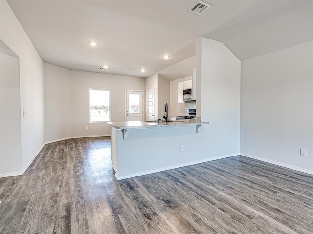 kitchen featuring dark wood-type flooring, white cabinetry, a kitchen breakfast bar, kitchen peninsula, and stove