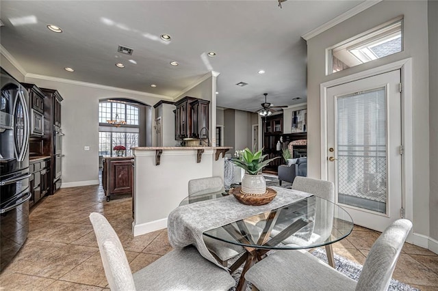 dining space with crown molding, ceiling fan, and a fireplace