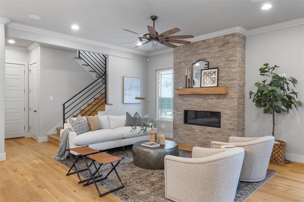 living room featuring crown molding, a stone fireplace, light hardwood / wood-style flooring, and ceiling fan