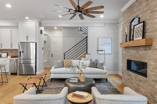 living room with ceiling fan, ornamental molding, a fireplace, and light hardwood / wood-style flooring