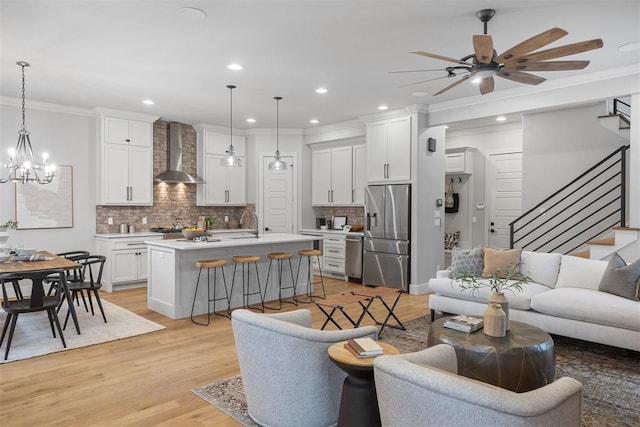 living room featuring ornamental molding, sink, ceiling fan with notable chandelier, and light wood-type flooring