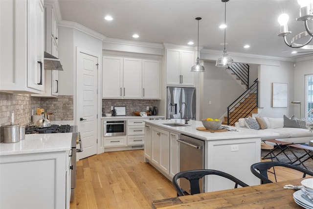 kitchen with decorative light fixtures, sink, white cabinets, stainless steel appliances, and a center island with sink