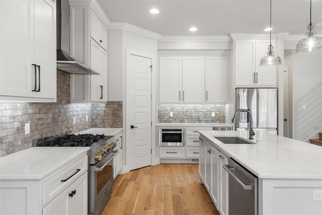 kitchen with wall chimney exhaust hood, sink, white cabinetry, hanging light fixtures, and stainless steel appliances