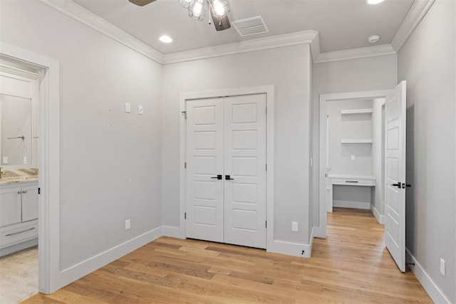 unfurnished bedroom with light wood-type flooring, ornamental molding, ceiling fan, ensuite bath, and a closet